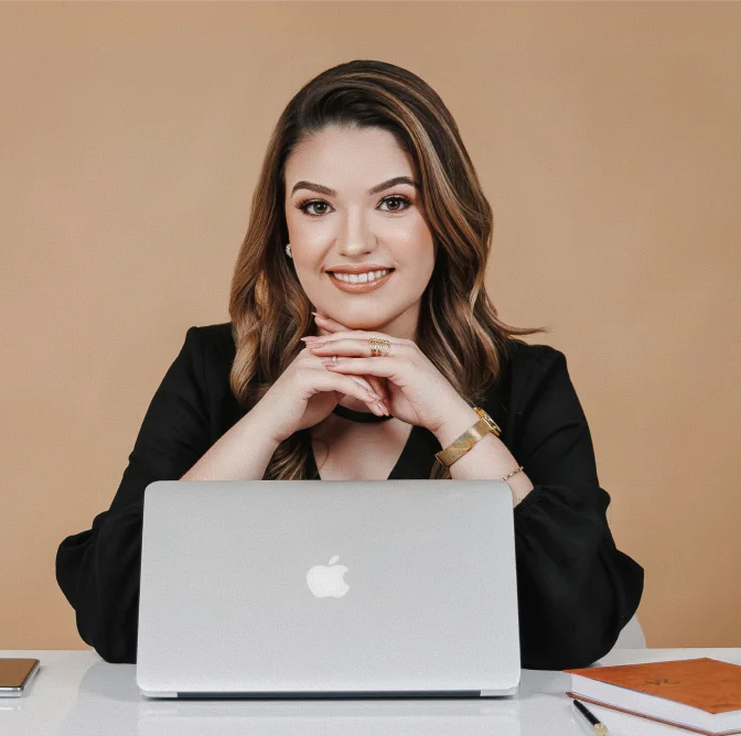 Advogada Bruna Garbulha Pereira sorridente sentada à mesa com notebook, em atendimento jurídico profissional e personalizado no escritório de advocacia
